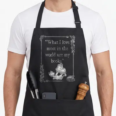 Book belle apron - White line art of girl reading with teapot and books inside floral frame with quote — shown on a black cotton canvas apron against a white background