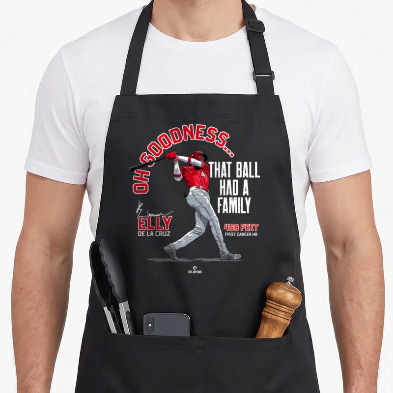 Ball family aprons - Elly De La Cruz swinging bat with OH GOODNESS THAT BALL HAD A FAMILY text in red and white — shown on a black cotton canvas apron against a white background