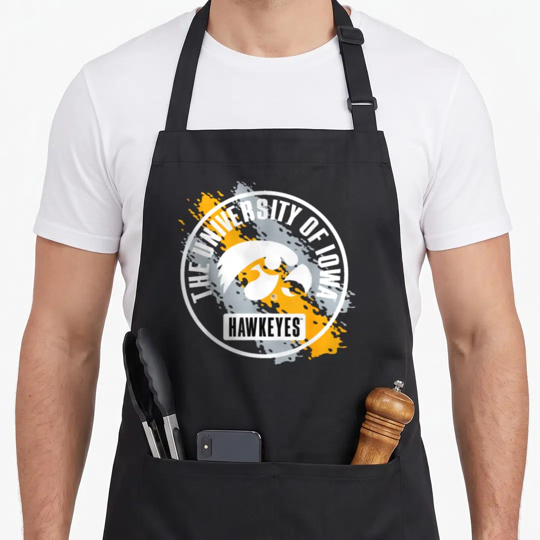 Iowa paint apron - University of Iowa hawk head logo with yellow splatters and HAWKEYES text — shown on a black cotton canvas apron against a white background