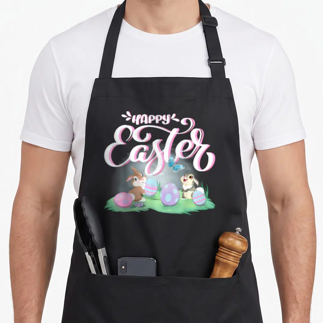 Bambi bunny apron - HAPPY Easter text above two bunnies, four eggs, and blue butterfly on grass — shown on a black cotton canvas apron against a white background