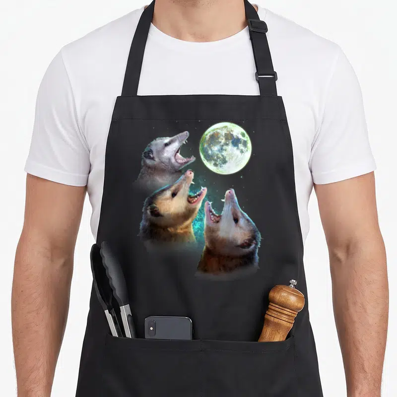 Three moon funny apron - Three realistic opossums howling at a full moon in grey and blue — shown on a black cotton canvas apron against a white background