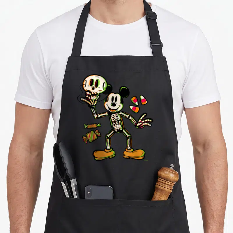 Treat skeleton halloween apron - Cartoon skeleton Mickey Mouse holding skull with candy corn and wrapped sweets — shown on a black cotton canvas apron against a white background