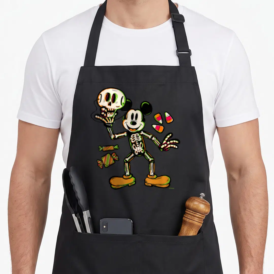 Treat skeleton halloween apron - Cartoon skeleton Mickey Mouse holding skull with candy corn and wrapped sweets — shown on a black cotton canvas apron against a white background
