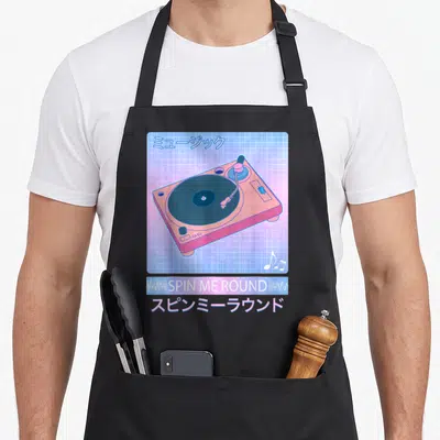 Record 80s apron - Pink turntable on blue grid with SPIN ME ROUND text and Japanese characters — shown on a black cotton canvas apron against a white background