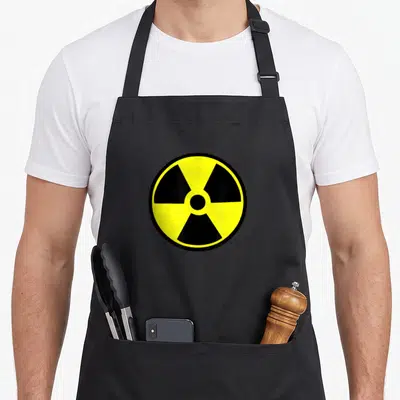Nuclear radiation aprons - Circular yellow and black radiation symbol centered on fabric — shown on a black cotton canvas apron against a white background