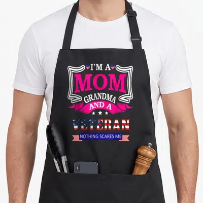 Funny veteran grandma apron - Stacked text I'm a Mom Grandma and a Veteran Nothing Scares Me with pink banner and flag — shown on a black cotton canvas apron against a white background
