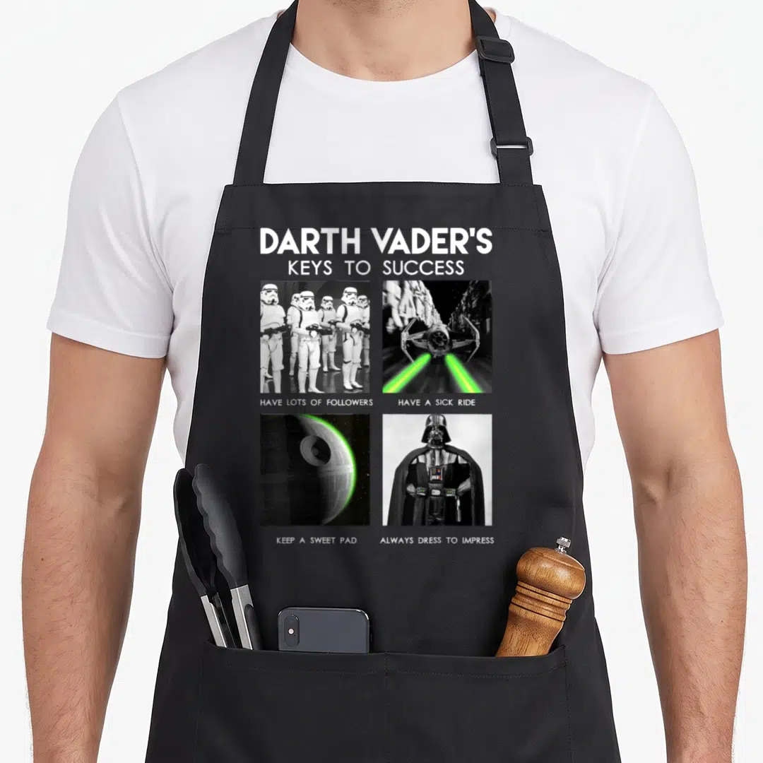 Vader key apron - Darth Vader graphic with four panels showing troopers, TIE fighter, Death Star, and armor — shown on a black cotton canvas apron against a white background