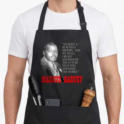 Marcus pride apron - Grayscale portrait of Marcus Garvey beside white quote text and red name on grey background — shown on a black cotton canvas apron against a white background