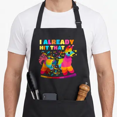Mayo cinco apron - Broken rainbow piñata with candies and text I already hit that — shown on a black cotton canvas apron against a white background