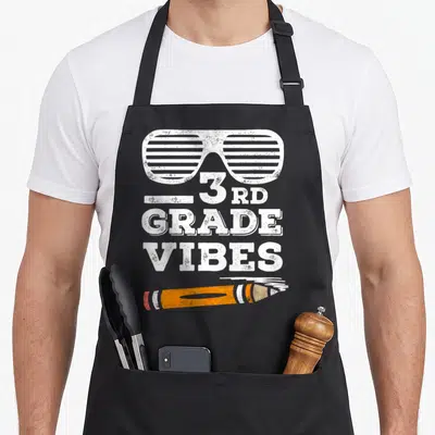 Third grade apron - Sunglasses, 3RD GRADE VIBES text, orange pencil, distressed white lettering — shown on a black cotton canvas apron against a white background