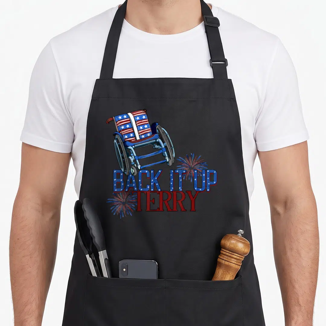 Terry reverse firework 4th of july apron - Wheelchair with flag pattern and BACK IT UP TERRY text surrounded by red — shown on a black cotton canvas apron against a white background