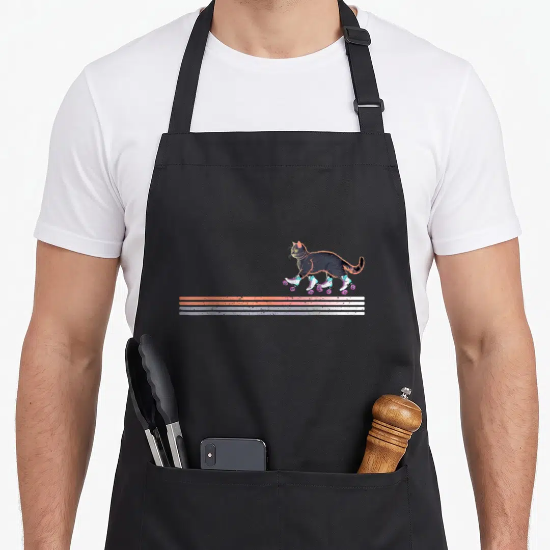 Roller cat apron - Dark grey cat on roller skates above three orange and blue stripes — shown on a black cotton canvas apron against a white background