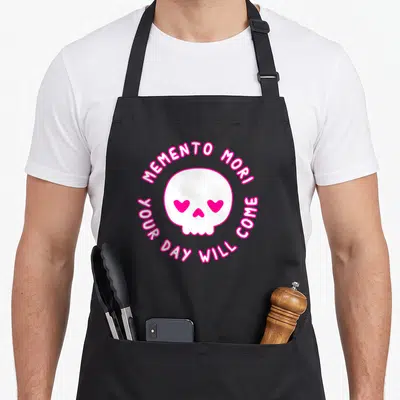 Memento goth apron - White skull with pink heart eyes and MEMENTO MORI text — shown on a black cotton canvas apron against a white background