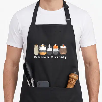 Celebrate theme aprons - Five cartoon guinea pigs in varied colors standing in a row above white text — shown on a black cotton canvas apron against a white background