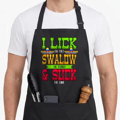 Lick i love tequila apron - Stacked text I LICK THE SALT SWALLOW THE TEQUILA & SUCK THE LIME with two sombreros — shown on a black cotton canvas apron against a white background