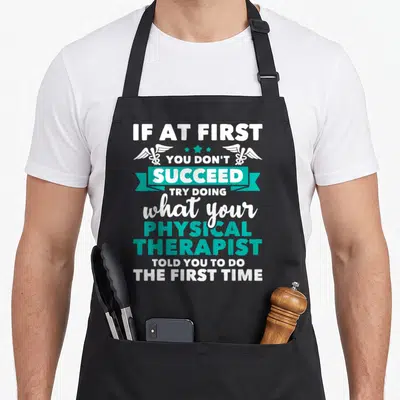 Physical therapist apron - White and teal stacked text with caducei symbols and ribbon reading IF AT FIRST YOU DON — shown on a black cotton canvas apron against a white background