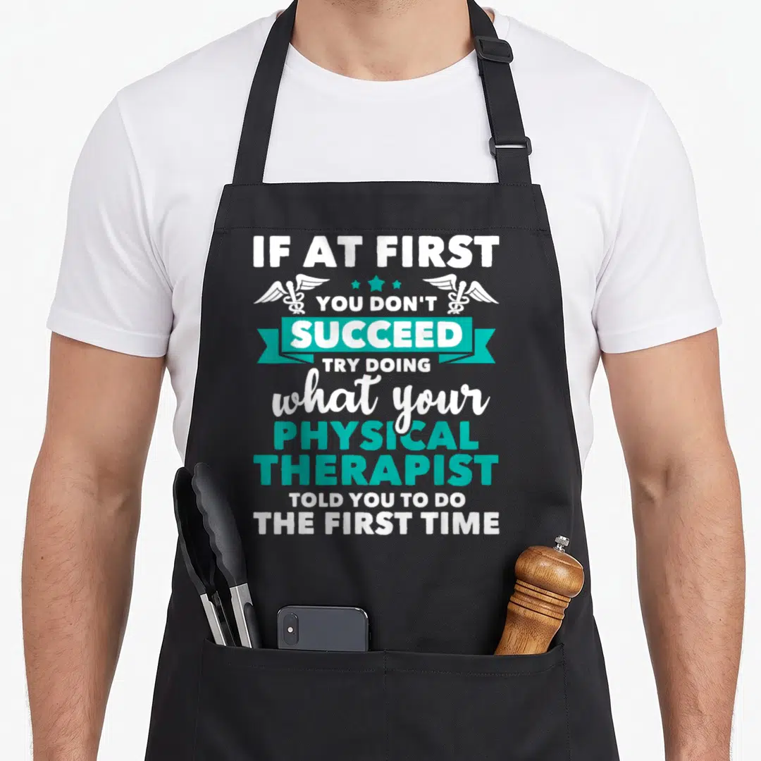 Physical therapist apron - White and teal stacked text with caducei symbols and ribbon reading IF AT FIRST YOU DON — shown on a black cotton canvas apron against a white background