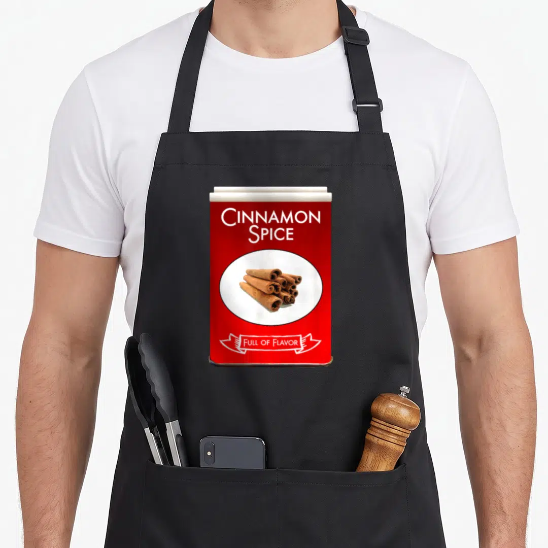 Costume spice apron - Red spice canister with brown cinnamon sticks and white text on white oval — shown on a black cotton canvas apron against a white background