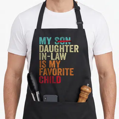 Son mom and daughter aprons - My Daughter In Law Is My Favorite Child text with crossed out Son in teal beige orange red — shown on a black cotton canvas apron against a white background