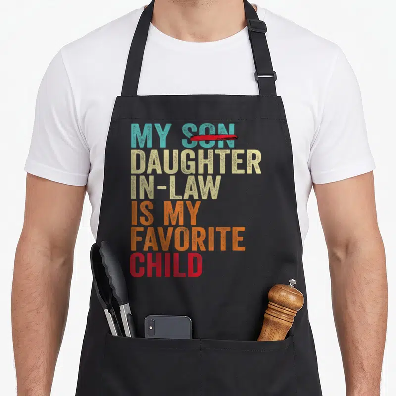 Son mom and daughter aprons - My Daughter In Law Is My Favorite Child text with crossed out Son in teal beige orange red — shown on a black cotton canvas apron against a white background