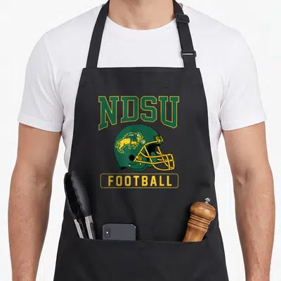 North football apron - Green football helmet with yellow bison and NDSU FOOTBALL text in cartoon style — shown on a black cotton canvas apron against a white background