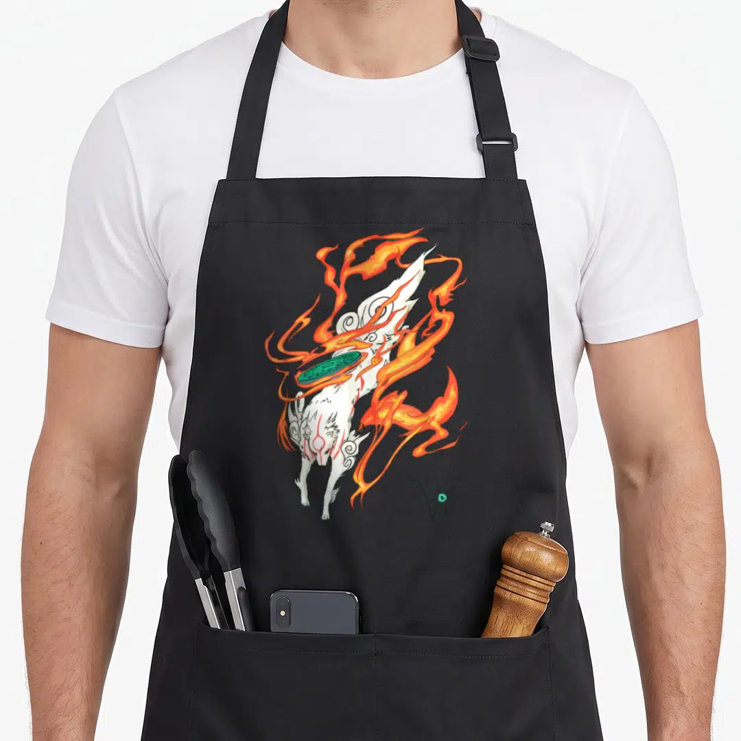Amaterasu video game apron - White fox diving with orange fire and green disk in cartoon style — shown on a black cotton canvas apron against a white background