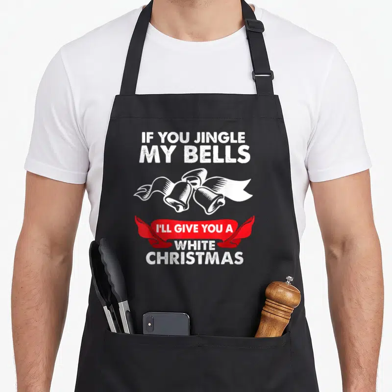 Jingle x apron - Two white bells tied with ribbon below text IF YOU JINGLE MY BELLS above a red banner reading I'll — shown on a black cotton canvas apron against a white background
