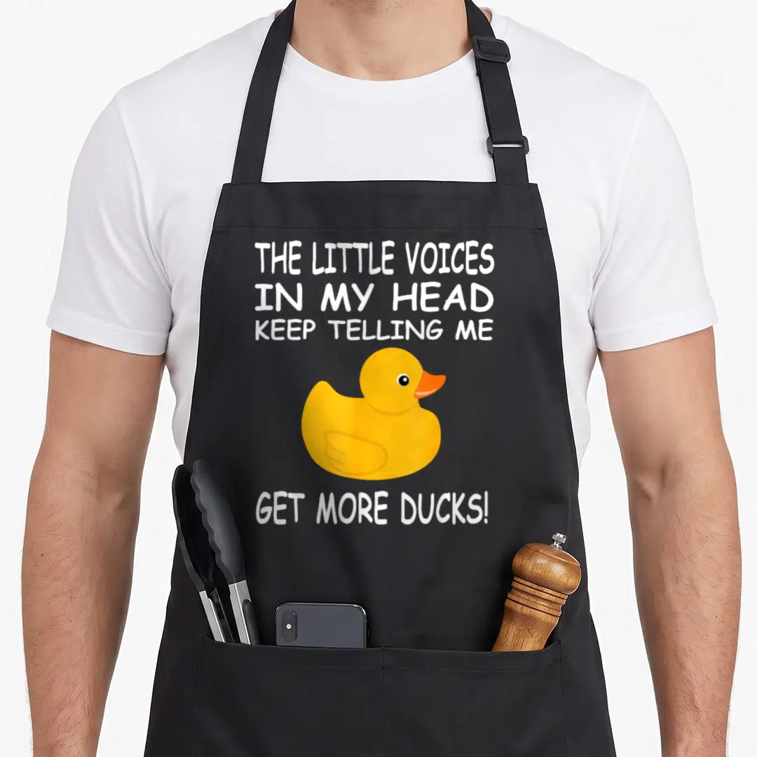 Voice duck apron - Yellow rubber duck illustration with white text about little voices telling the wearer to get more — shown on a black cotton canvas apron against a white background