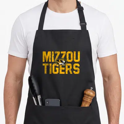 Missouri distressed apron - Yellow MIZZOU TIGERS text with overlapping black and white tiger head logo in distressed — shown on a black cotton canvas apron against a white background