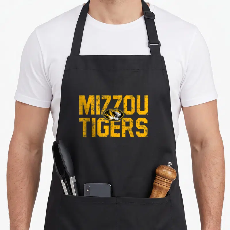Missouri distressed apron - Yellow MIZZOU TIGERS text with overlapping black and white tiger head logo in distressed — shown on a black cotton canvas apron against a white background