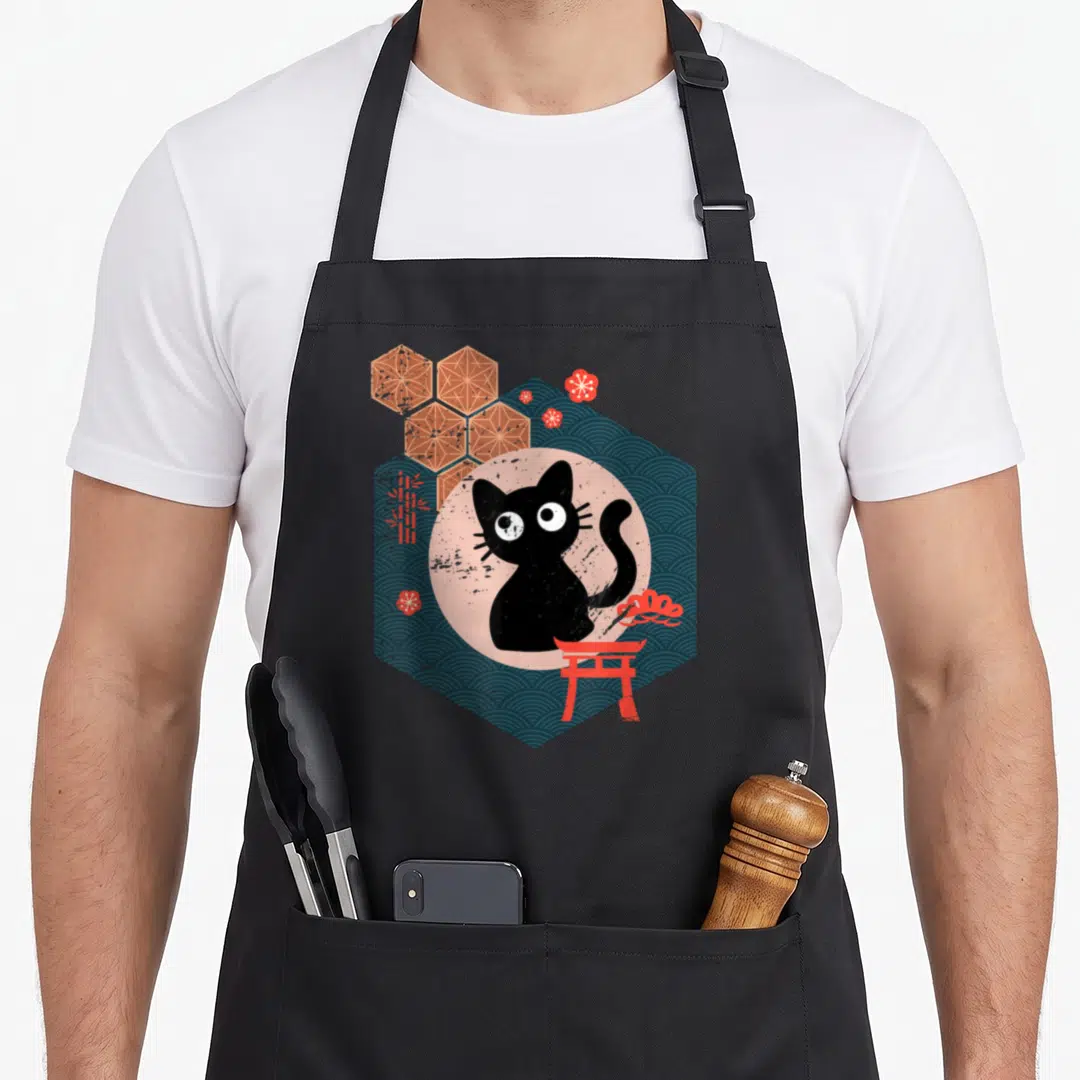 Lifestyle cat apron - Black cat in pink circle inside dark blue hexagon with red torii gate and blossoms — shown on a black cotton canvas apron against a white background