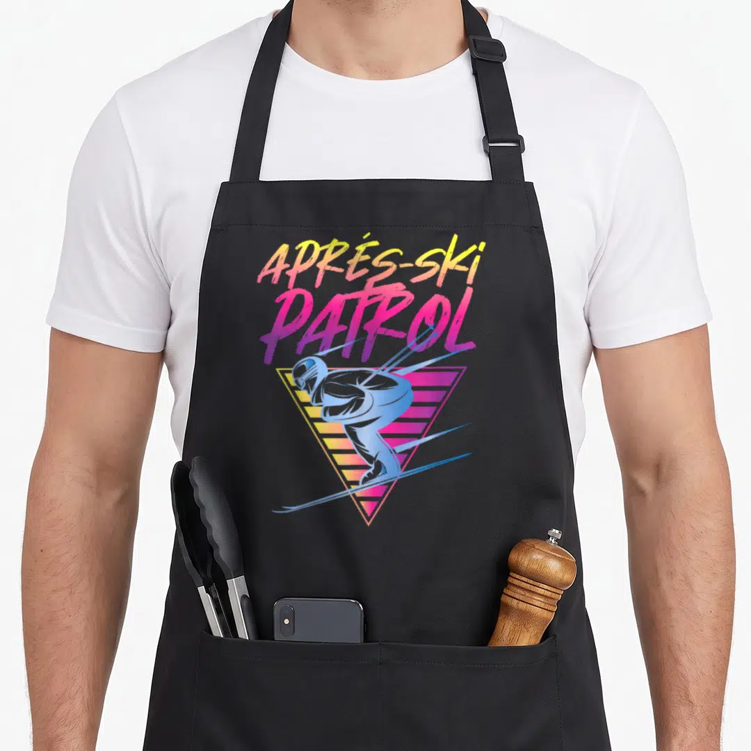 Apre 80s apron - Retro skier in blue crouching over a yellow and pink gradient triangle with stacked text — shown on a black cotton canvas apron against a white background