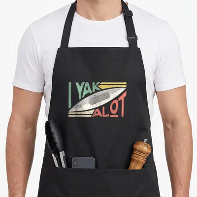 Kayak lot of aprons - Retro I YAK A LOT text with white kayak and horizontal speed lines in green red and yellow — shown on a black cotton canvas apron against a white background