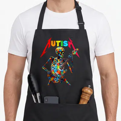 Player skeleton apron - Colorful puzzle-patterned skeleton playing electric guitar under arched AUTISM text — shown on a black cotton canvas apron against a white background