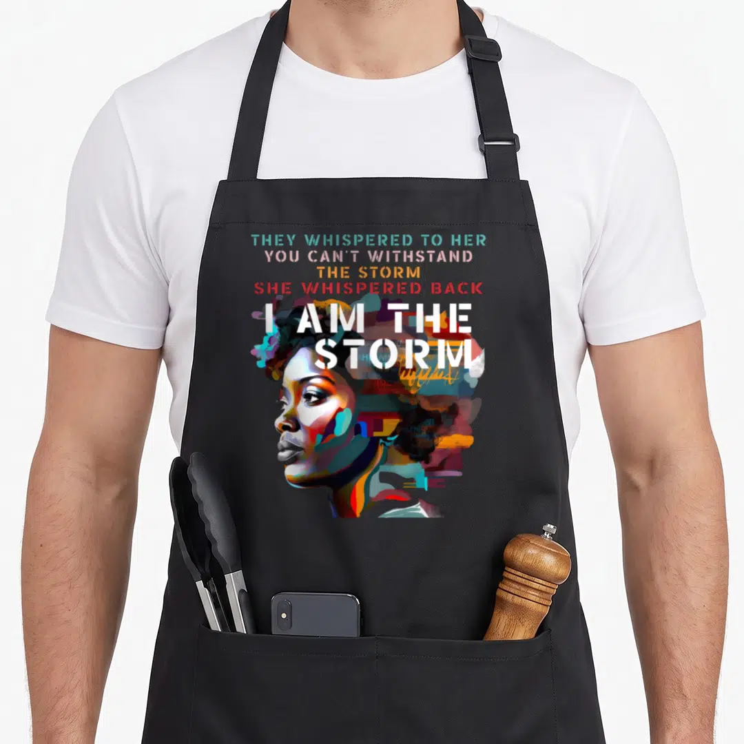 Storm african apron - Watercolor woman profile with multicolored hair and stacked text I Am The Storm — shown on a black cotton canvas apron against a white background