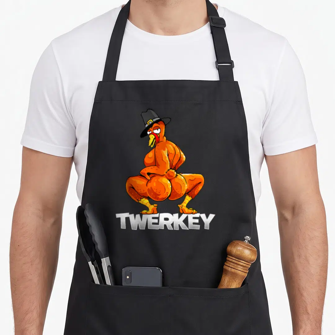 Twerkey pilgrim apron - Cartoon orange turkey in a black hat posing above white TWERKEY text — shown on a black cotton canvas apron against a white background