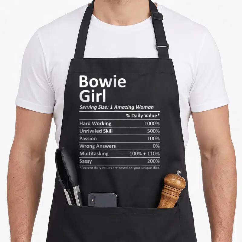 Bowie md apron - White nutrition label typography listing 1000% hard working and 200% sassy values on black fabric — shown on a black cotton canvas apron against a white background