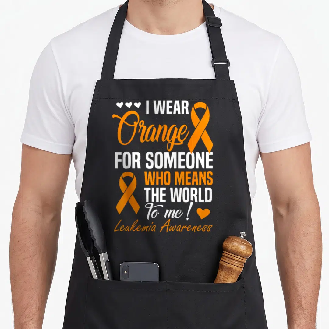Someone cancer awareness apron - I Wear Orange stacked text with two orange ribbons and white and orange hearts — shown on a black cotton canvas apron against a white background