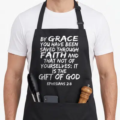 Ephesian scripture bible verse apron - Distressed white typography reading By Grace You Have Been Saved Through Faith — shown on a black cotton canvas apron against a white background