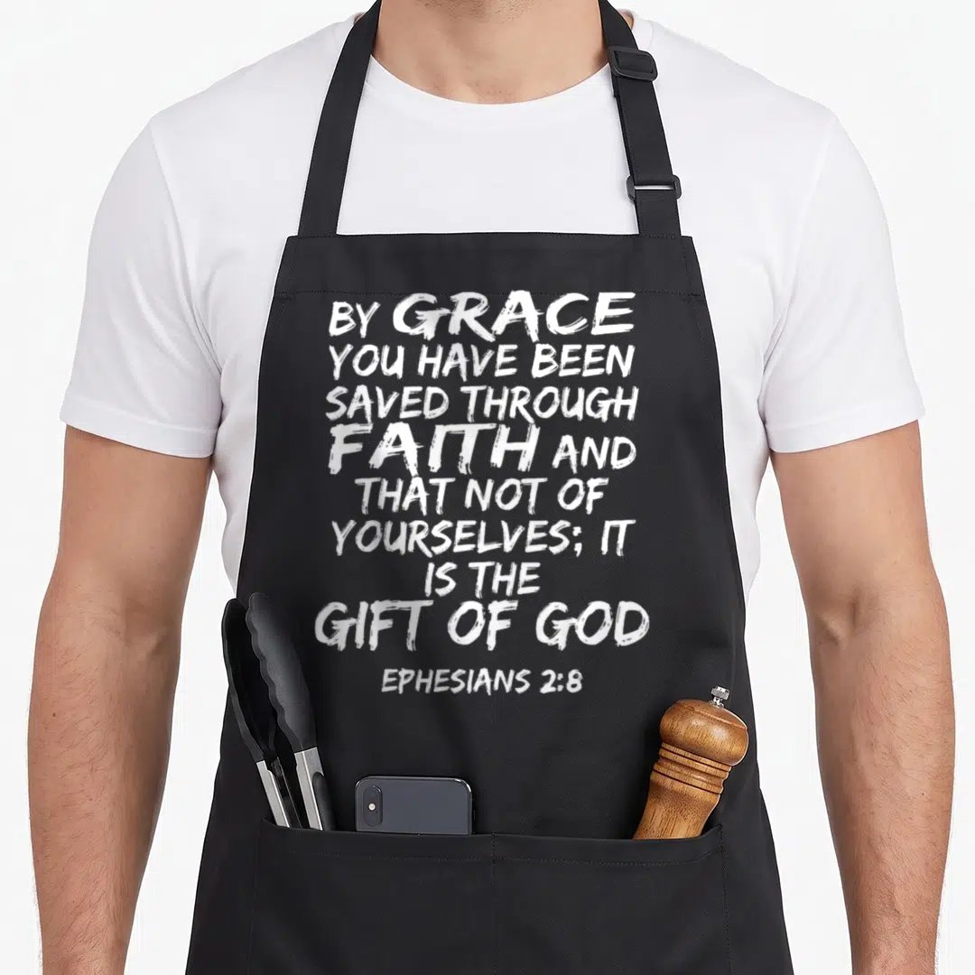 Ephesian scripture bible verse apron - Distressed white typography reading By Grace You Have Been Saved Through Faith — shown on a black cotton canvas apron against a white background