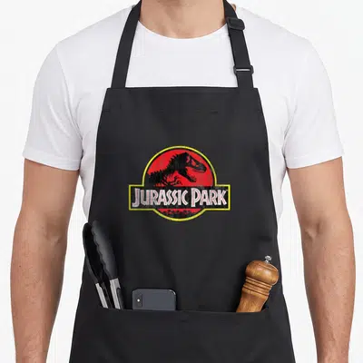 Funny original distressed apron - Dinosaur skeleton in red circle with Jurassic Park text and distressed texture — shown on a black cotton canvas apron against a white background