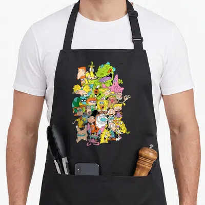 Complete character aprons - Dense cluster of yellow, pink, green, and blue cartoon characters overlapping on a black — shown on a black cotton canvas apron against a white background