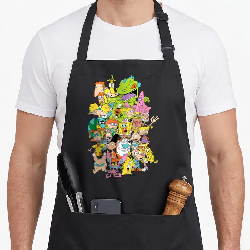 Complete character aprons - Dense cluster of yellow, pink, green, and blue cartoon characters overlapping on a black — shown on a black cotton canvas apron against a white background
