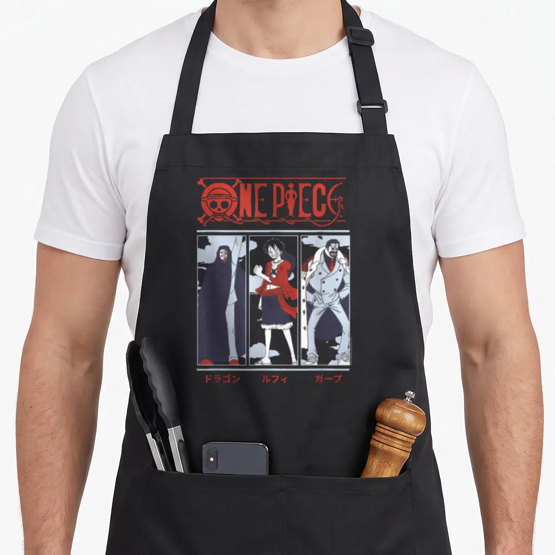 Meet anime apron - ONE PIECE logo above three panels of Dragon, Luffy, and Garp with Japanese text labels below each — shown on a black cotton canvas apron against a white background