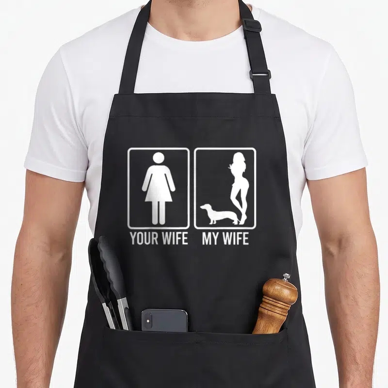 Dachshund personalized dog apron - White YOUR WIFE MY WIFE text with dachshund silhouette next to generic female symbol — shown on a black cotton canvas apron against a white background