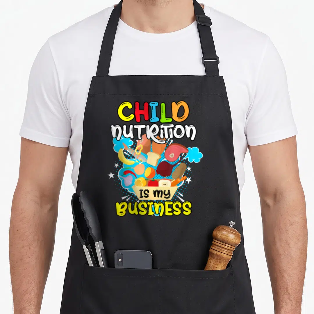 Business cafeteria aprons - Colorful cartoon food cluster with blue clouds and text reading Child Nutrition Is My — shown on a black cotton canvas apron against a white background