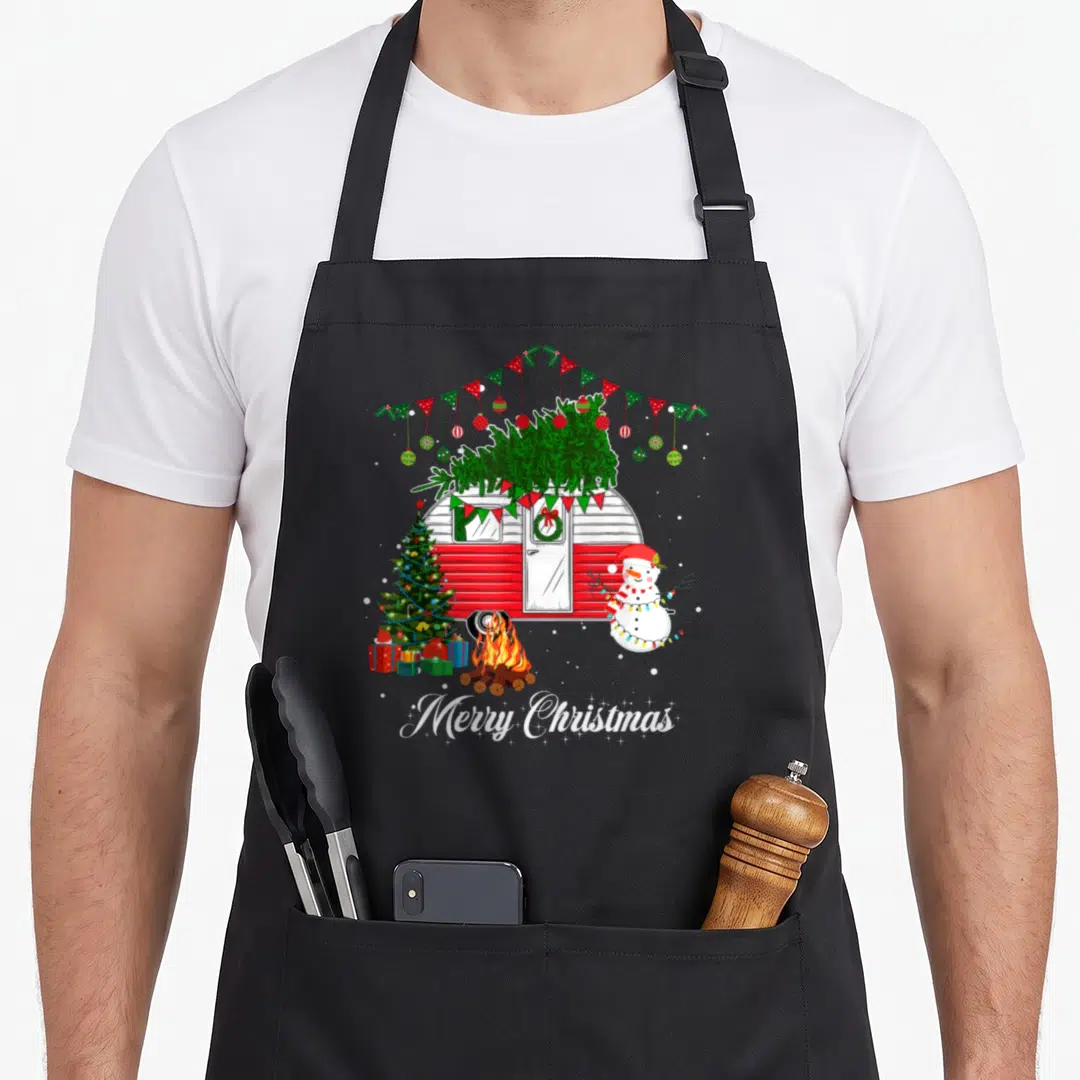 Camper christmas tree apron - Red camper with green tree, snowman, campfire, and Merry Christmas text in cartoon style — shown on a black cotton canvas apron against a white background
