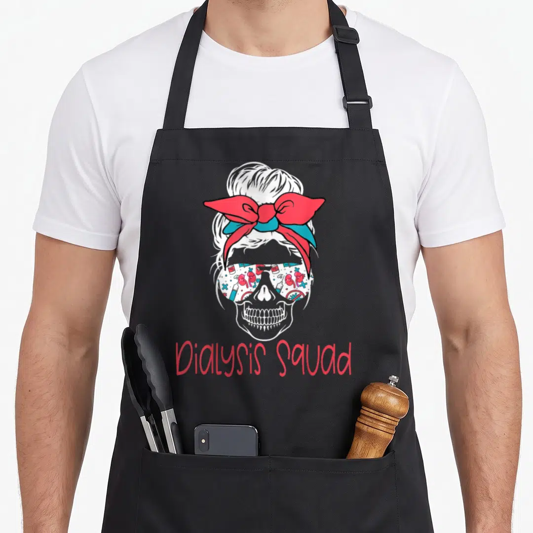 Hemodialysis nurse apron - White skull with red teal bow, medical icon sunglasses, red Dialysis Squad text below — shown on a black cotton canvas apron against a white background