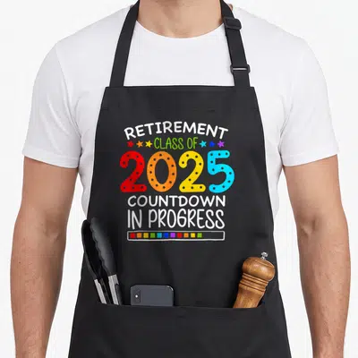 Countdown teacher apron - Colorful 2025 retirement countdown text with loading bar and stars — shown on a black cotton canvas apron against a white background