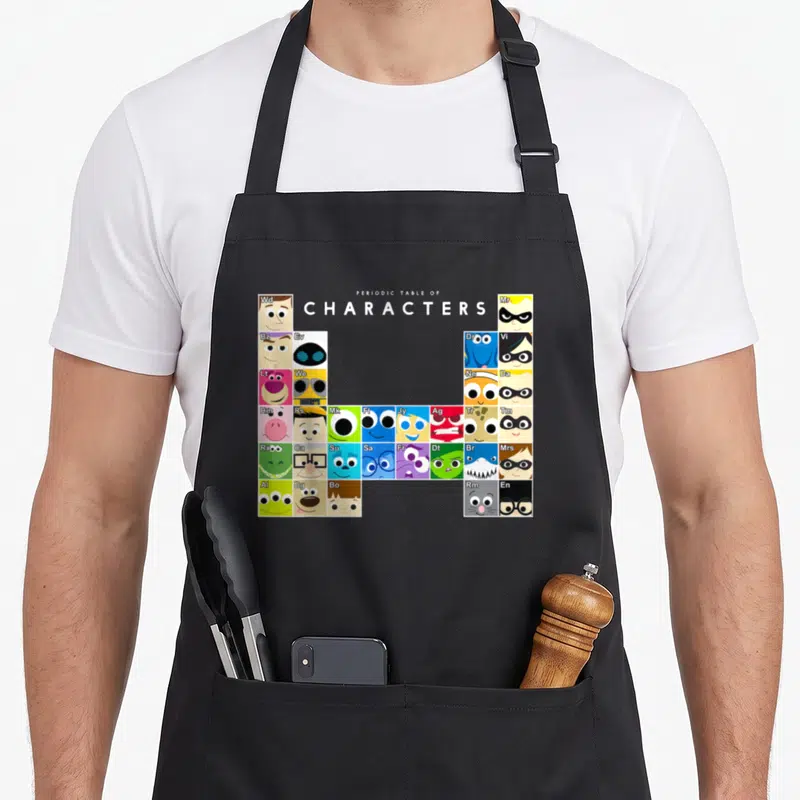 Collection table apron - Grid of colorful character faces with two-letter symbols arranged under centered text — shown on a black cotton canvas apron against a white background